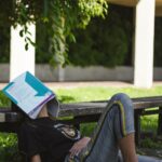 une étudiante se relaxe dans un parc avec un livre sur le visage, à l'ombre d'un arbre